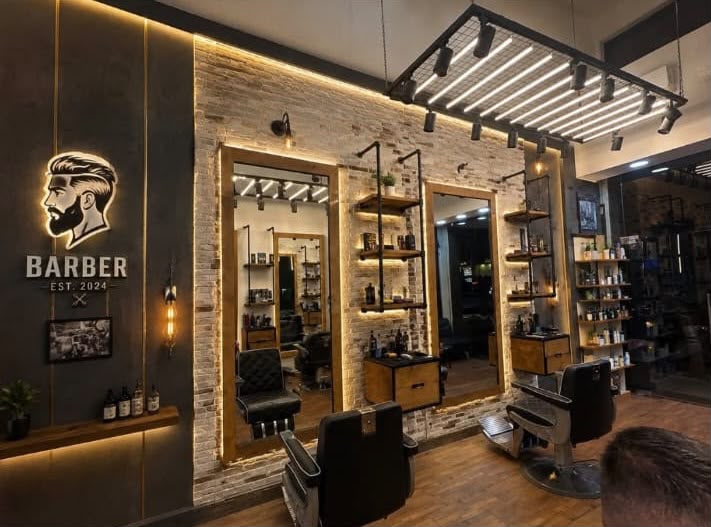 The Moe Badrani barbershop interior — warm lighting, stone-clad wall, leather chairs, mirrors and the illuminated BARBER sign